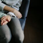 sitting woman in gray long sleeved shirt holding baby s hand in blue long sleeved shirt; symbolizes parental alienation