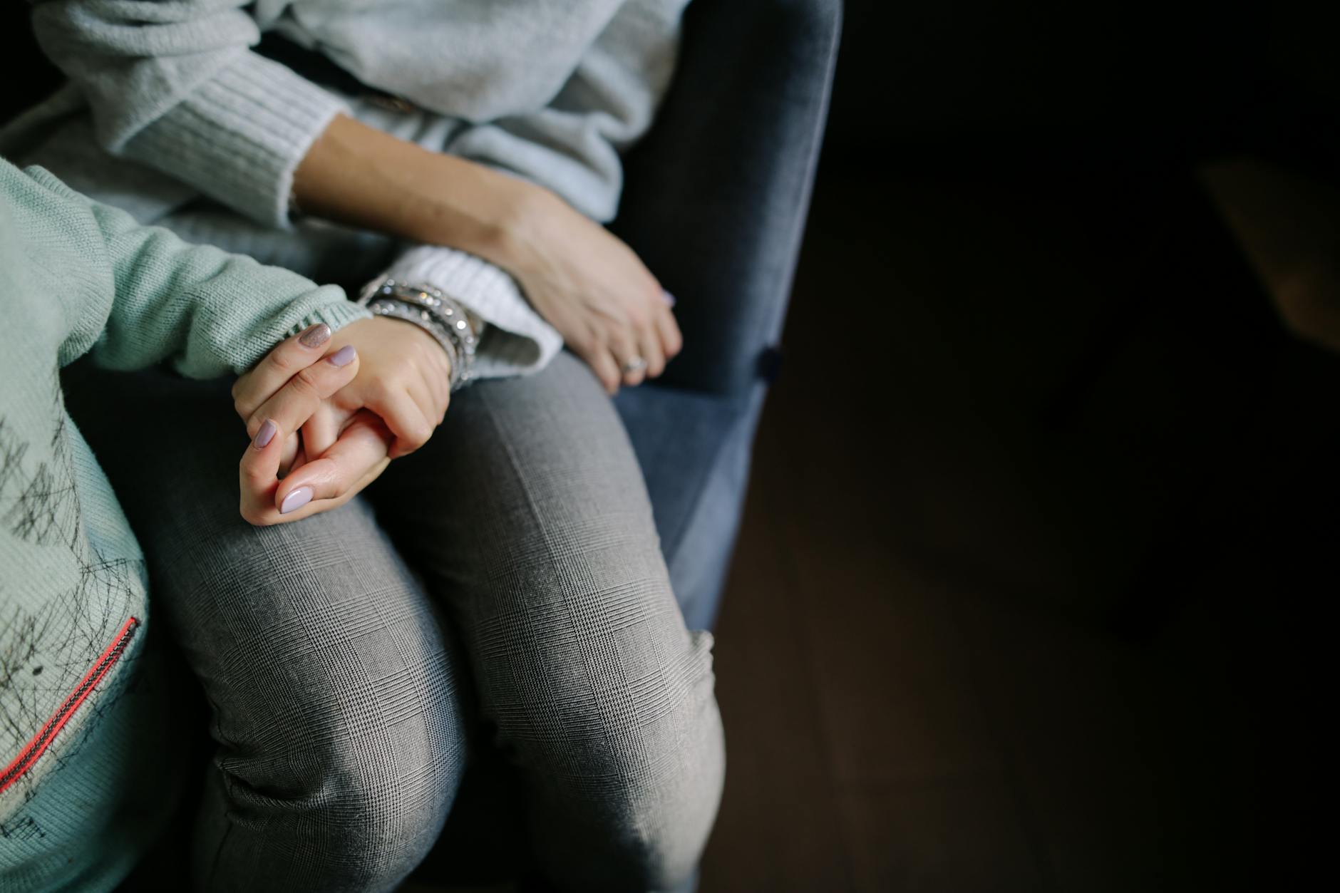 sitting woman in gray long sleeved shirt holding baby s hand in blue long sleeved shirt; symbolizes parental alienation